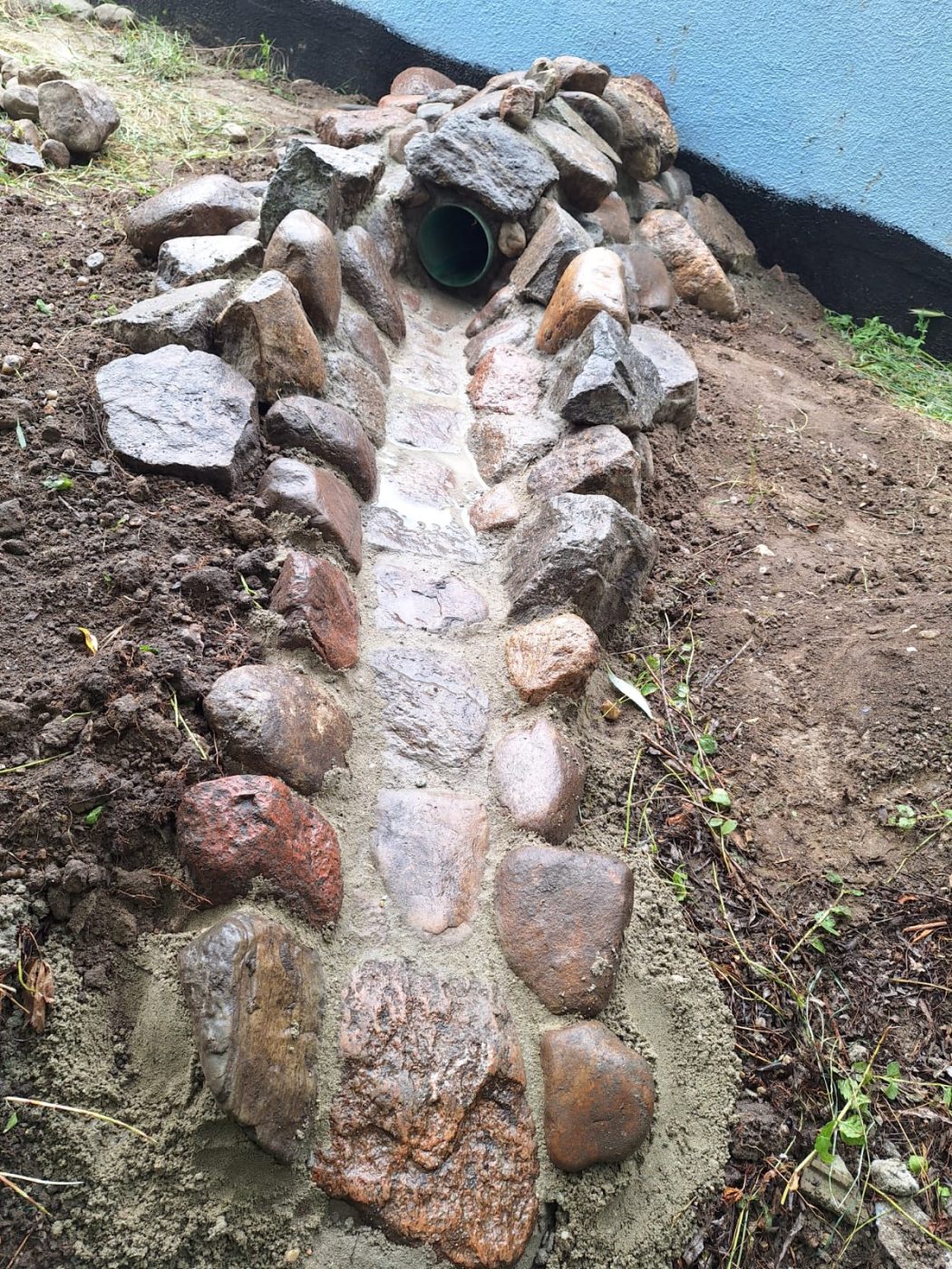 Detail einer gemauerten Natursteinrinne mit Ablaufrohr